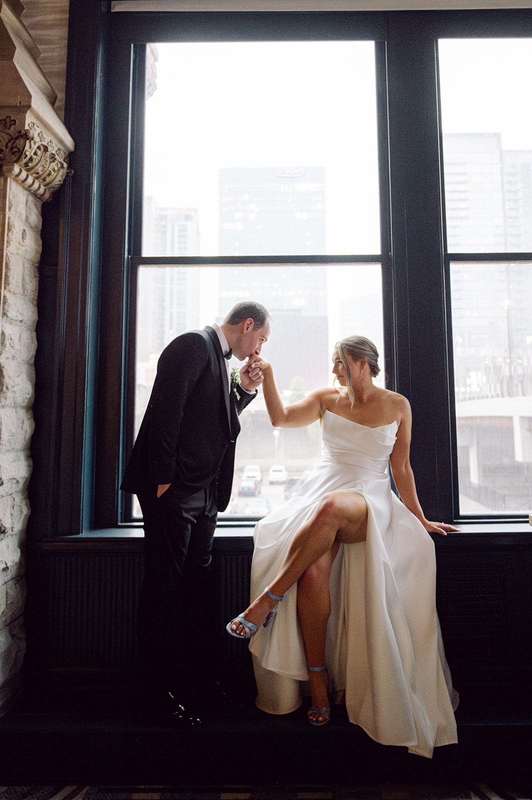 Romantic wedding portrait of groom kissing bride's hand by large window.