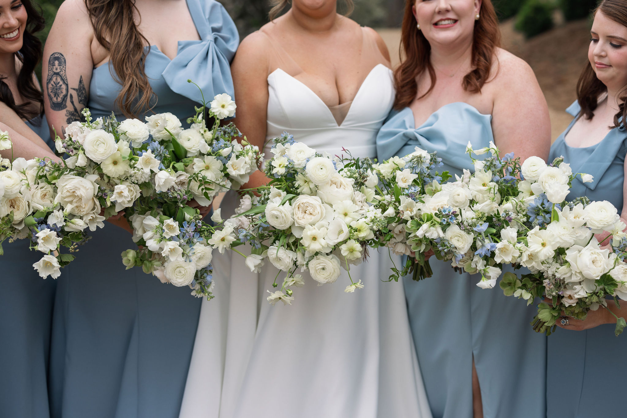 bride with bridesmaids in blue dresses holding white and blue bouquets
