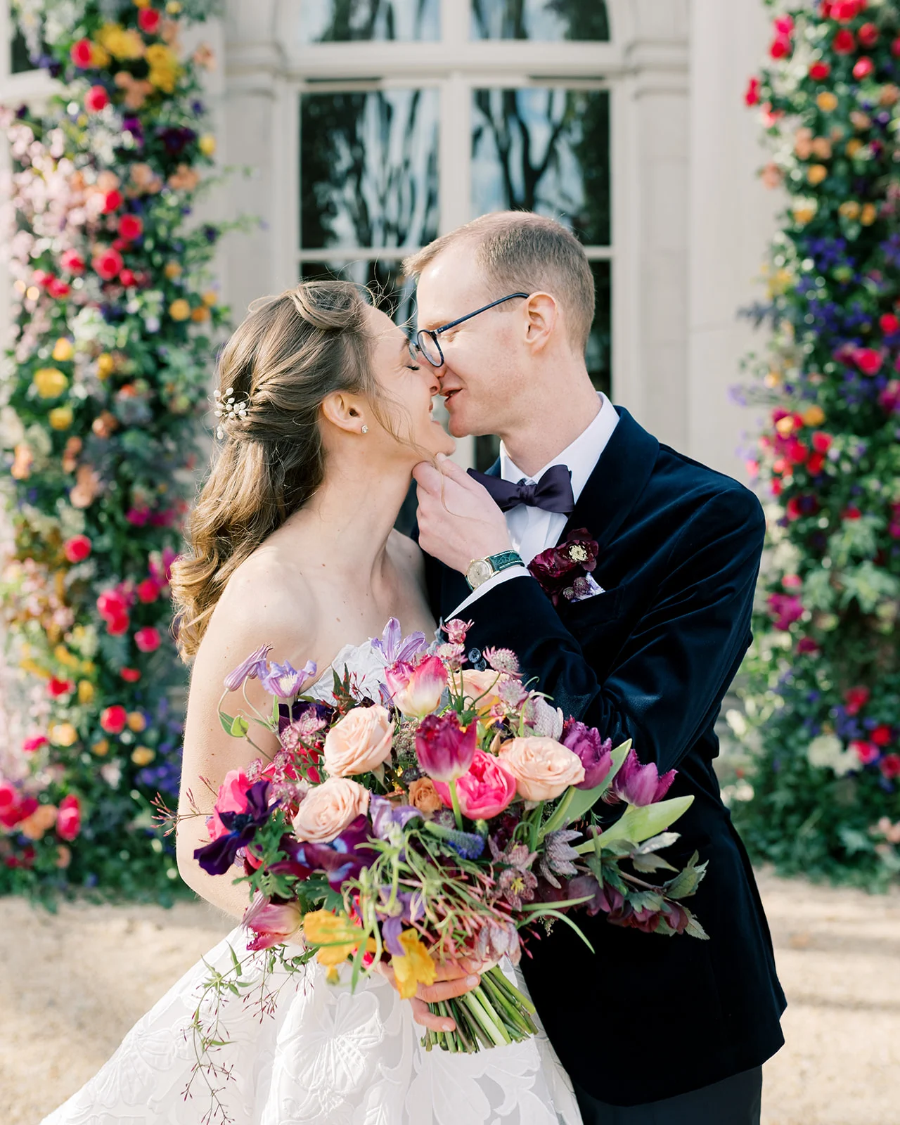 newlyweds kiss while bride holds colorful bouquet of flowers 