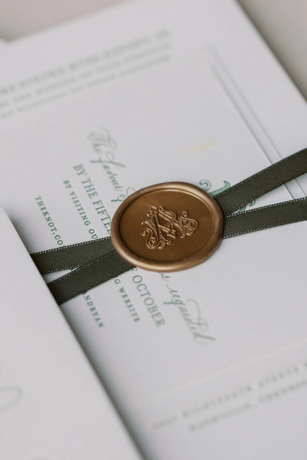 dark green ribbon and wax seal hold invitation suite together 