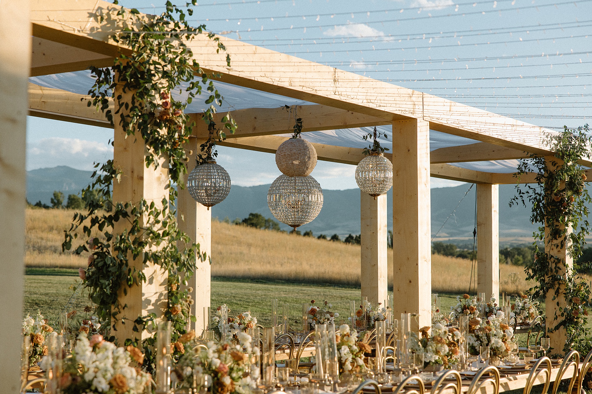 lighting and greenery decorate wood beams framing outdoor reception space 