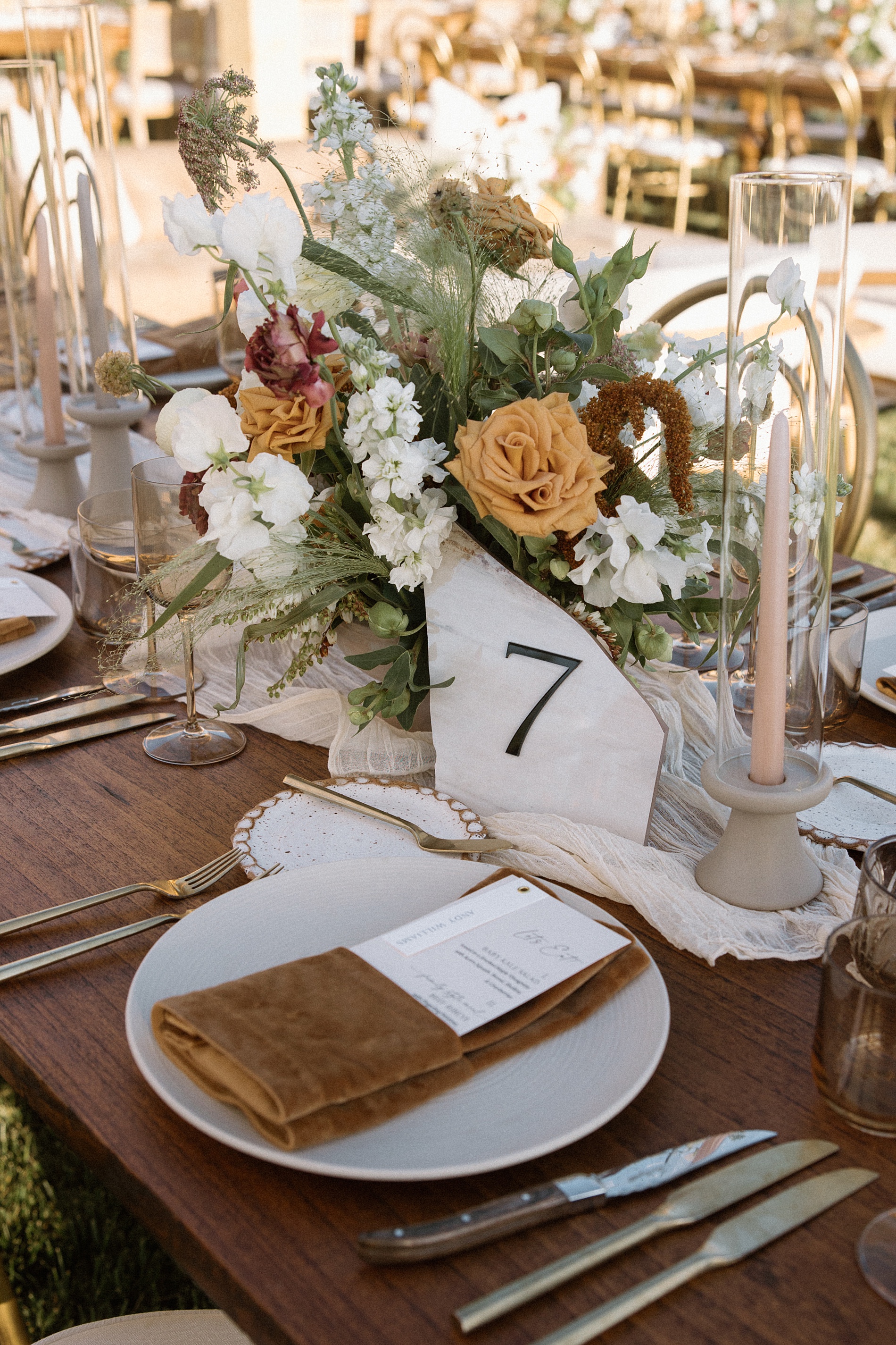 tablescape at wedding featuring slanted edge stone table numbers with custom menus wrapped in suede leather napkin