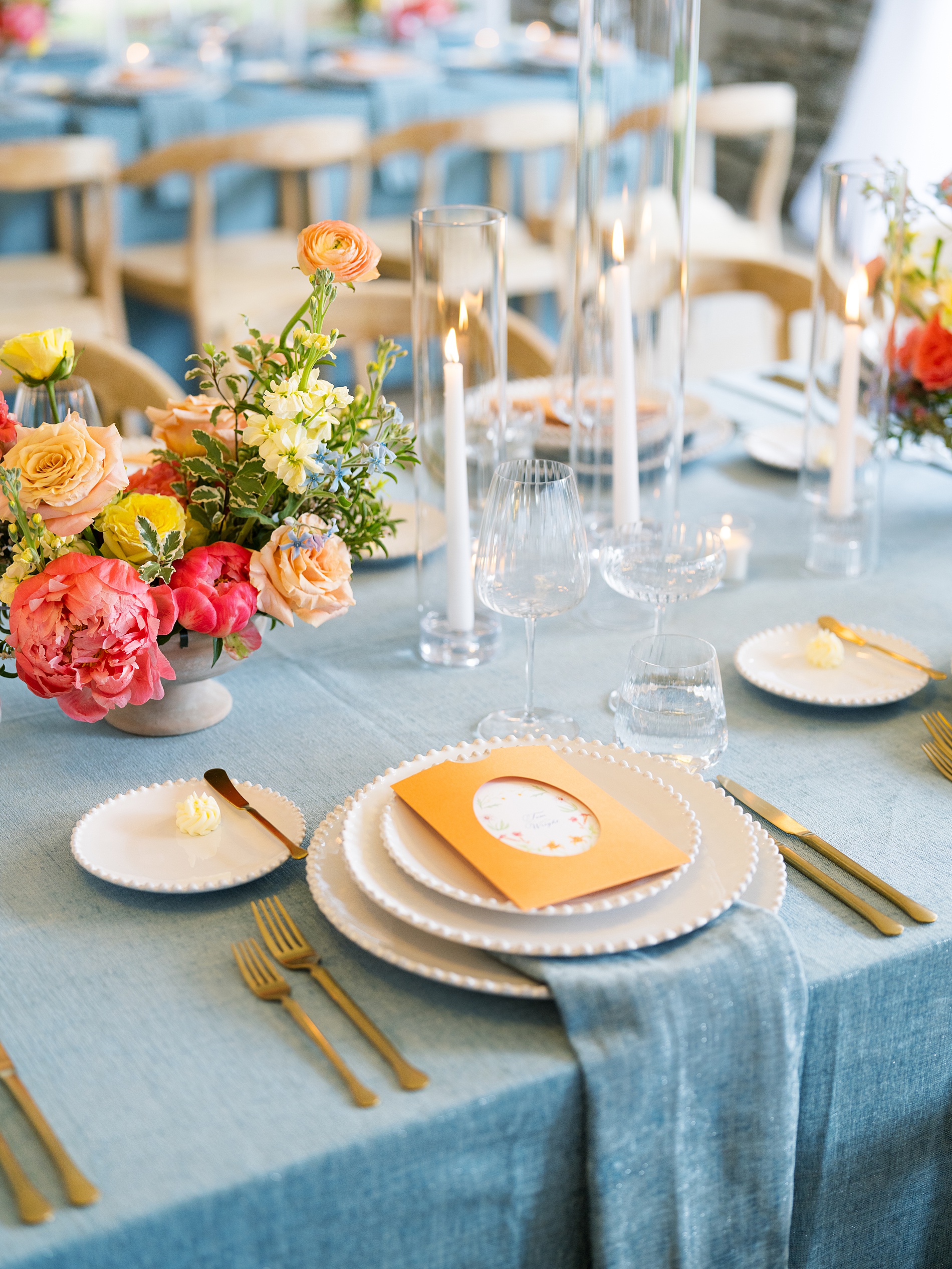 Artistic and Colorful Wedding details with orange and floral wedding menus on white plates sitting blue tablecloth 