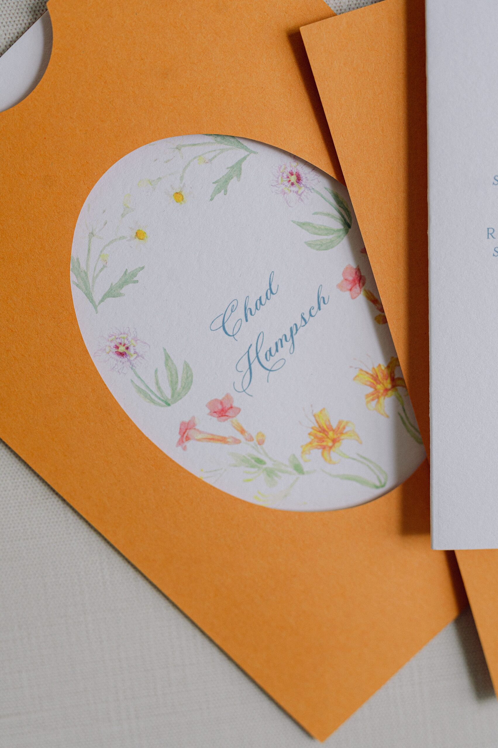 hand painted floral artwork on wedding menus tucked into a custom die-cut orange pocket