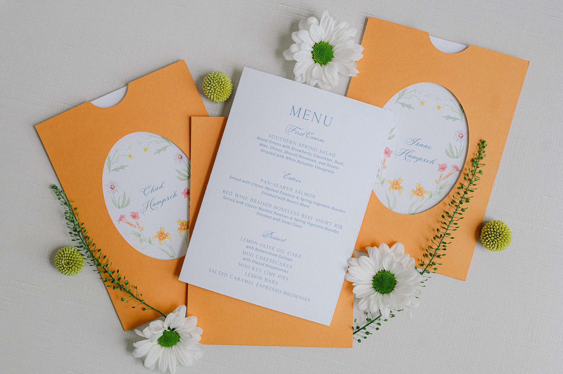 artistic and colorful wedding details and paper goods with floral artwork on place cards and menu tucked into orange die cut pockets 