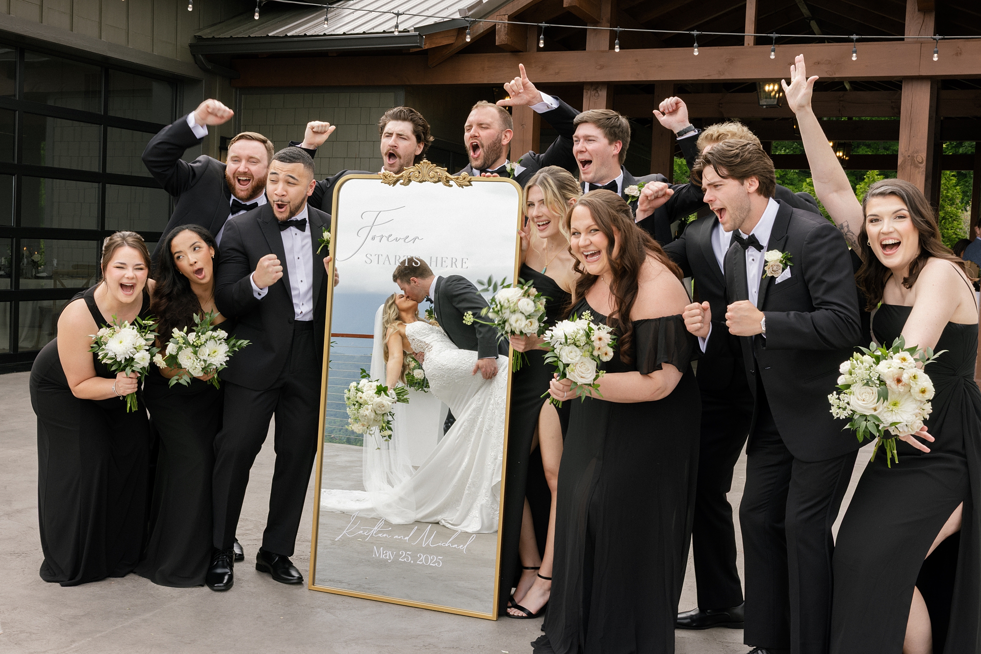wedding party cheer as bride and groom kiss and their reflection is seen in mirrored welcome sign