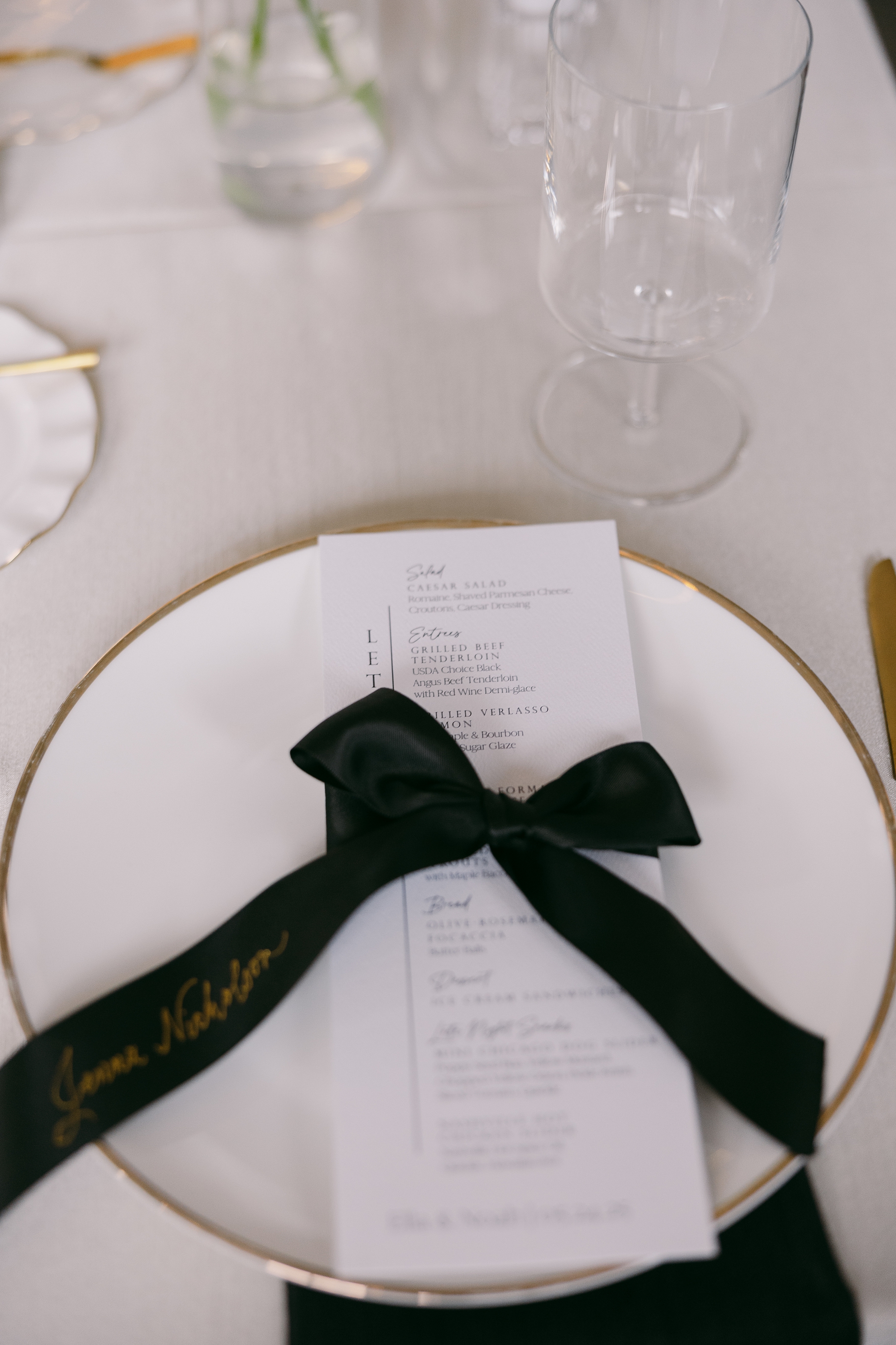 black satin ribbon place cards tied around white menus at place setting 