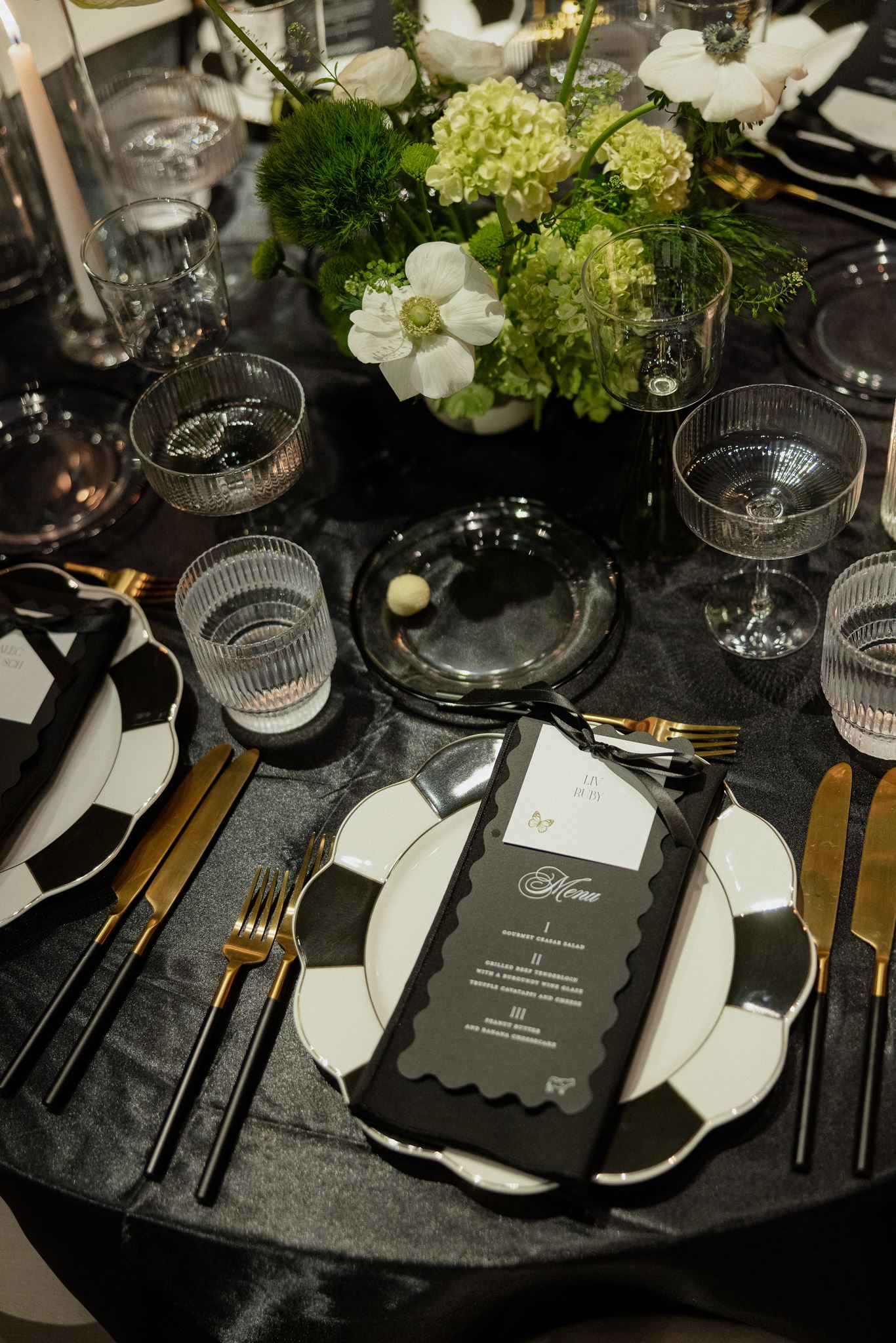 wavy die cut black menus with white place card attached by black ribbon sitting on white plate with black accents  created by Nashville wedding design house, White Ink Calligraphy 